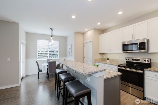kitchen featuring a center island, white cabinets, stainless steel appliances, and wood finished floors