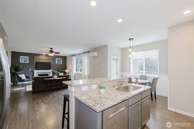kitchen featuring wood finished floors, an island with sink, a fireplace, gray cabinets, and a sink