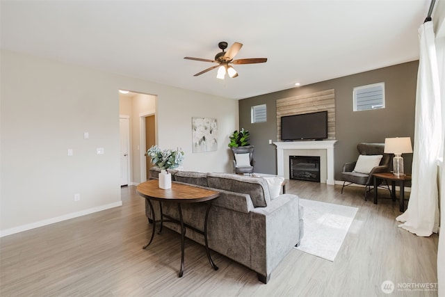 living area with light wood-style flooring, a fireplace, baseboards, and ceiling fan
