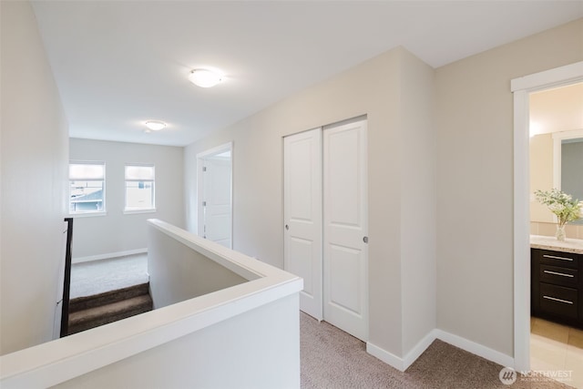 hallway with an upstairs landing, light colored carpet, and baseboards