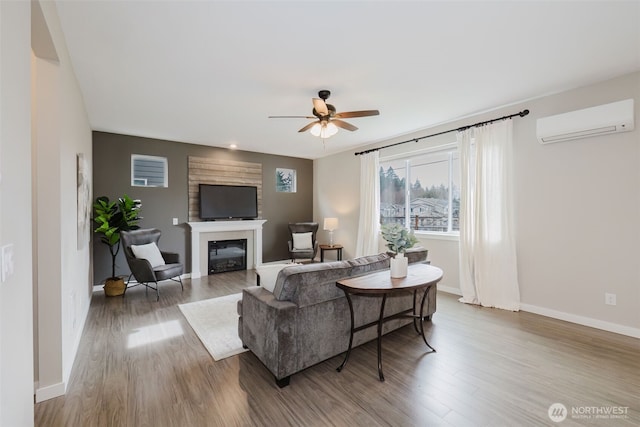 living room featuring baseboards, a wall mounted air conditioner, wood finished floors, a glass covered fireplace, and a ceiling fan