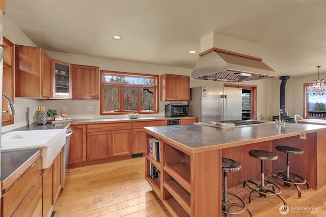 kitchen with island range hood, light wood-style flooring, brown cabinets, a kitchen breakfast bar, and stainless steel appliances