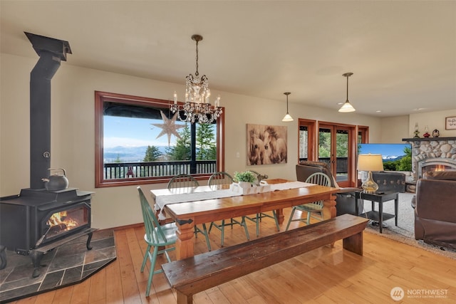 dining space featuring a stone fireplace, light wood-type flooring, a wood stove, and an inviting chandelier