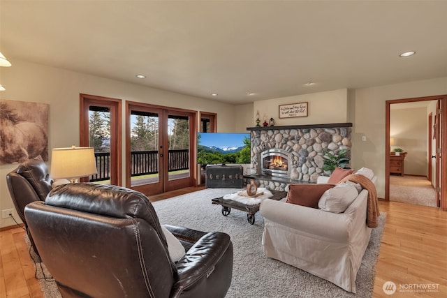 living room with a stone fireplace, french doors, light wood-type flooring, and recessed lighting