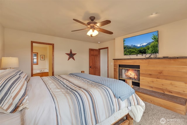 bedroom featuring ceiling fan, ensuite bathroom, and a glass covered fireplace