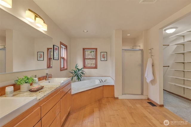 full bath with double vanity, a sink, a shower stall, wood finished floors, and a bath