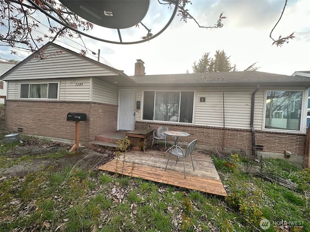 rear view of property featuring a chimney, a deck, and brick siding