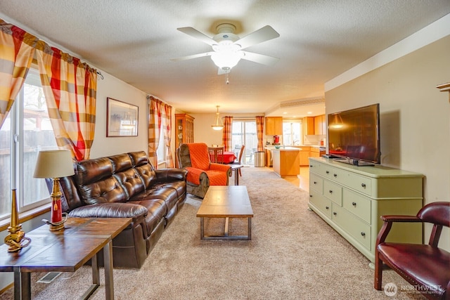 living area with ceiling fan, a textured ceiling, and light colored carpet