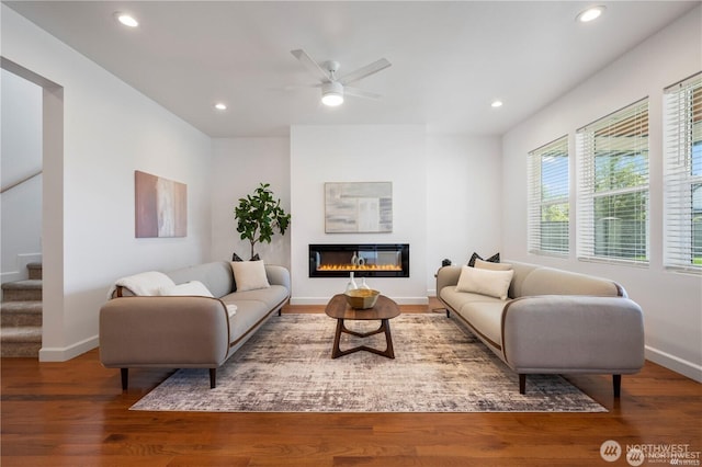 living area featuring wood finished floors, stairway, a glass covered fireplace, and recessed lighting