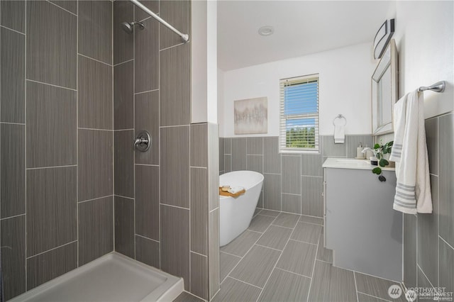 full bathroom featuring a wainscoted wall, tile walls, a freestanding bath, a tile shower, and vanity