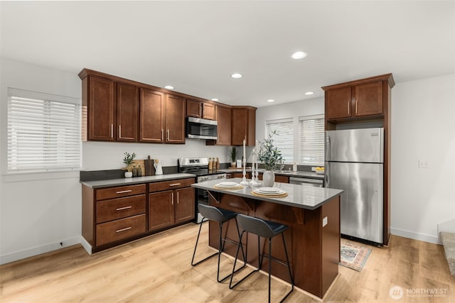 kitchen featuring recessed lighting, a kitchen island, appliances with stainless steel finishes, light wood-type flooring, and a kitchen bar