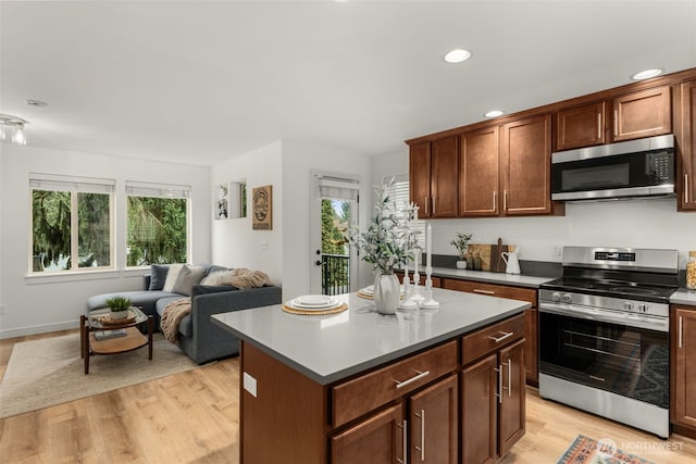 kitchen featuring light wood finished floors, a kitchen island, open floor plan, stainless steel appliances, and light countertops