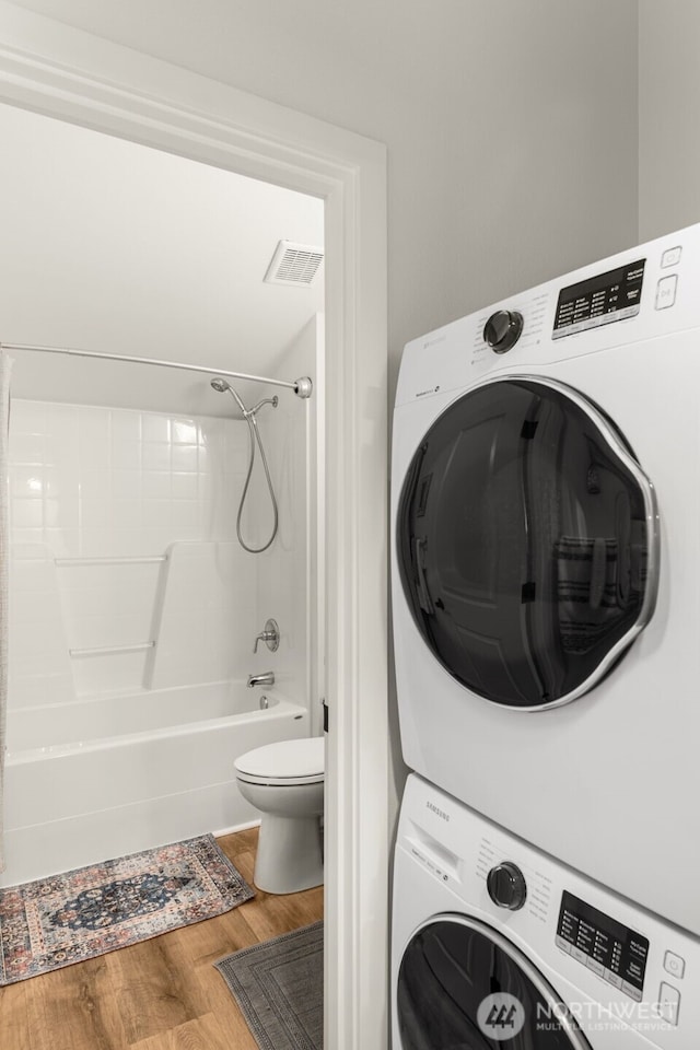 washroom with stacked washer / dryer, wood finished floors, and visible vents