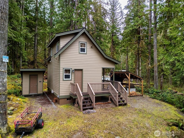 back of property with a storage shed, stairway, a view of trees, and an outdoor structure