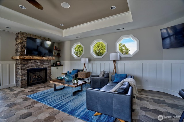 living area featuring recessed lighting, a fireplace, a ceiling fan, wainscoting, and a tray ceiling