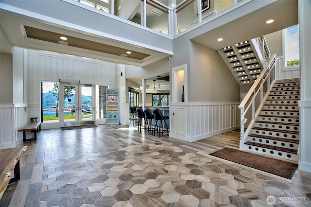 foyer featuring stairs, a high ceiling, a decorative wall, and french doors