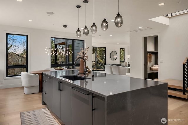 kitchen with light wood finished floors, decorative light fixtures, an island with sink, recessed lighting, and a sink