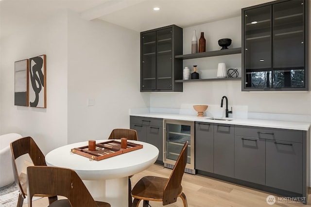 kitchen with gray cabinetry, light wood-style flooring, beverage cooler, a sink, and light countertops