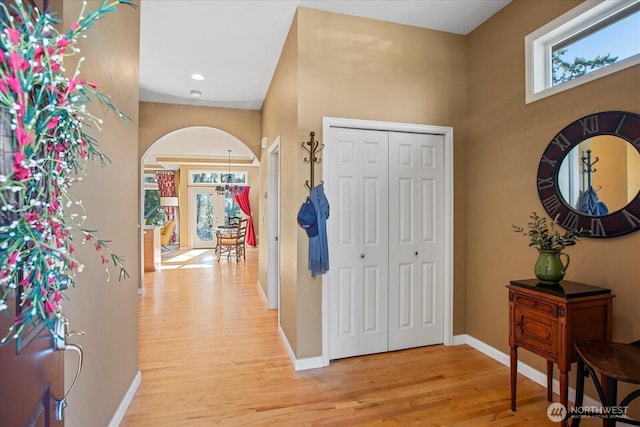 entrance foyer featuring arched walkways, baseboards, plenty of natural light, and light wood finished floors