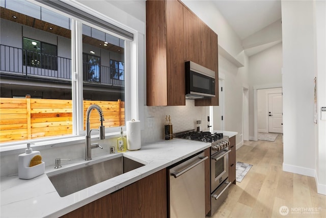 kitchen featuring tasteful backsplash, light wood-style flooring, appliances with stainless steel finishes, light stone counters, and a sink