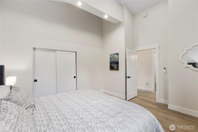 bedroom with a towering ceiling, light wood-type flooring, baseboards, and a closet