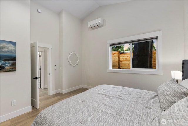 bedroom with high vaulted ceiling, an AC wall unit, light wood-style flooring, and baseboards