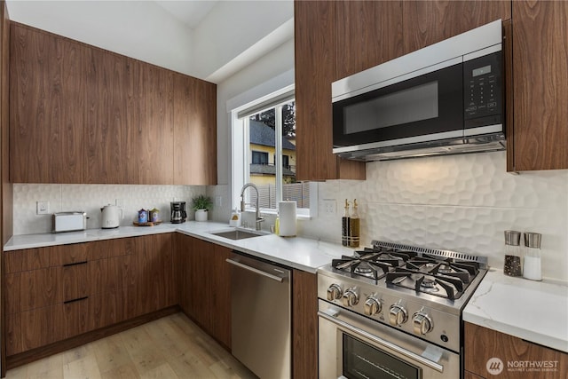 kitchen featuring stainless steel appliances, a sink, decorative backsplash, light wood finished floors, and modern cabinets