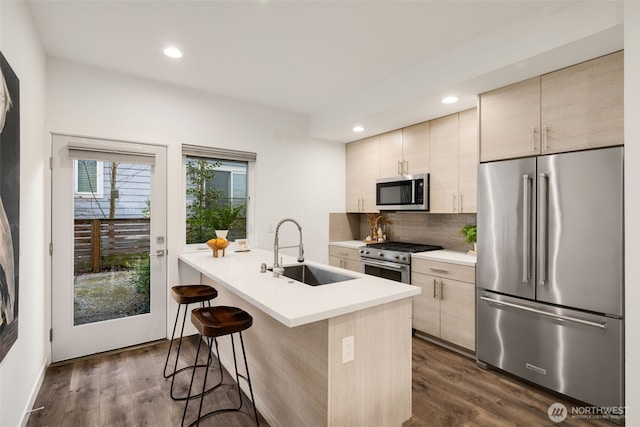 kitchen featuring premium appliances, light countertops, decorative backsplash, a sink, and a kitchen breakfast bar