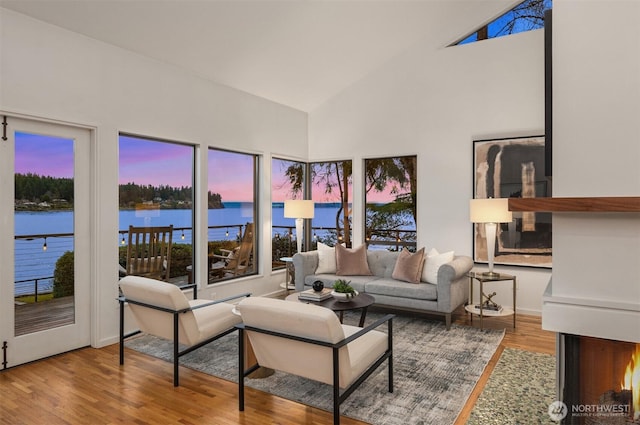 living area with high vaulted ceiling, a water view, and wood finished floors