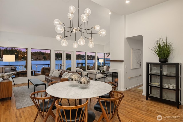 dining room featuring a water view, a towering ceiling, french doors, light wood finished floors, and a glass covered fireplace