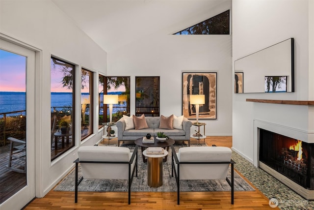 living room with a lit fireplace, high vaulted ceiling, a water view, and wood finished floors