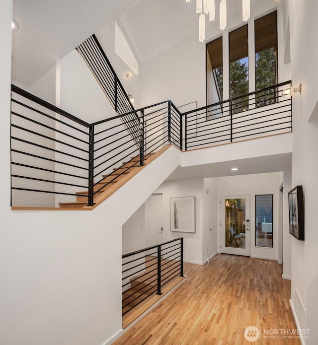 staircase featuring a high ceiling, wood finished floors, visible vents, and baseboards