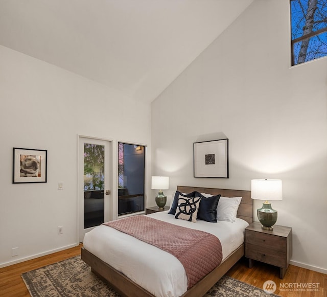 bedroom featuring access to outside, high vaulted ceiling, wood finished floors, and baseboards