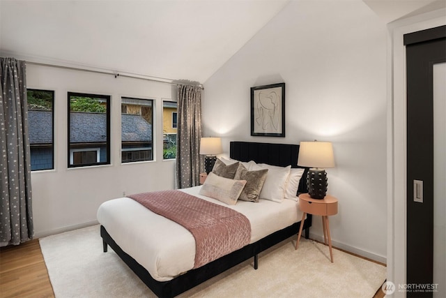 bedroom with lofted ceiling, light wood-style flooring, and baseboards