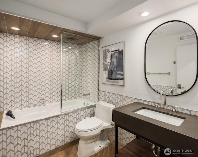 bathroom with toilet, recessed lighting, tiled shower / bath combo, a sink, and visible vents