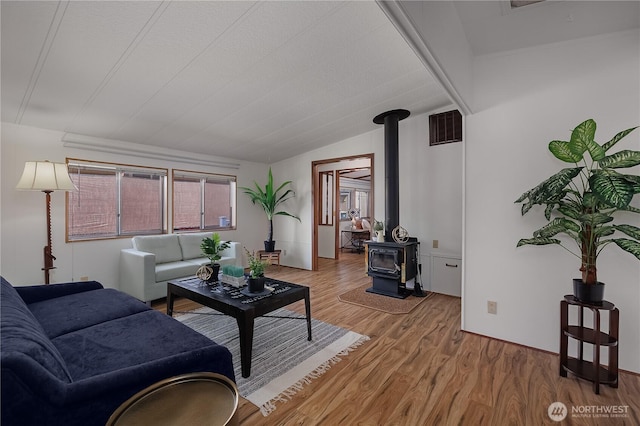 living room featuring visible vents, lofted ceiling, light wood-style floors, and a wood stove