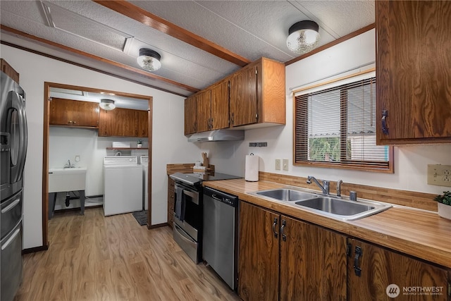 kitchen with under cabinet range hood, washing machine and dryer, lofted ceiling, stainless steel appliances, and a sink