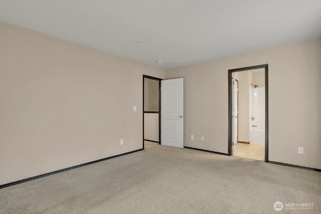 unfurnished bedroom featuring light carpet, connected bathroom, and baseboards