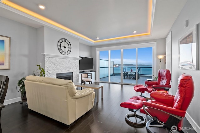 living area featuring a fireplace, a raised ceiling, dark wood finished floors, and baseboards