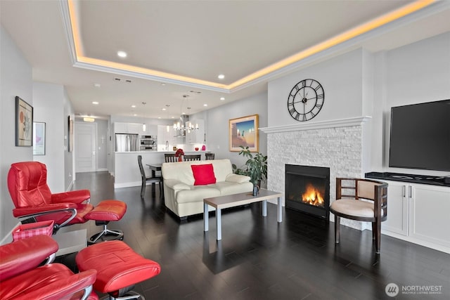 living room with a notable chandelier, recessed lighting, dark wood-type flooring, a fireplace, and a tray ceiling