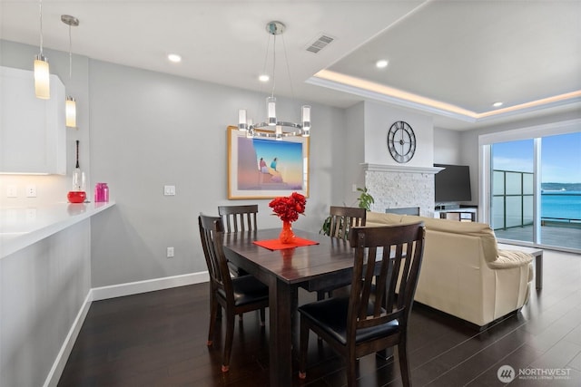 dining space with dark wood-style floors, a stone fireplace, visible vents, and baseboards