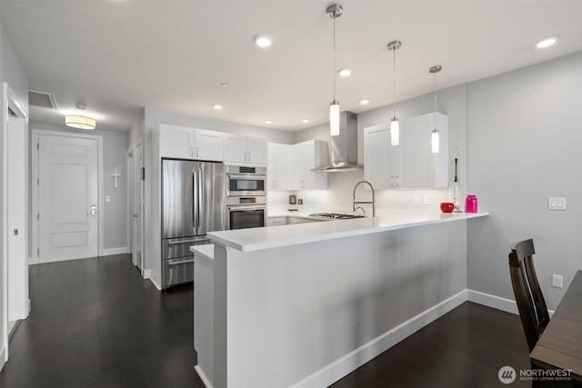 kitchen featuring a peninsula, stainless steel appliances, light countertops, wall chimney range hood, and white cabinetry