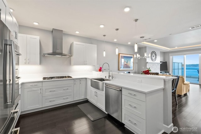 kitchen with visible vents, appliances with stainless steel finishes, a peninsula, wall chimney range hood, and a sink