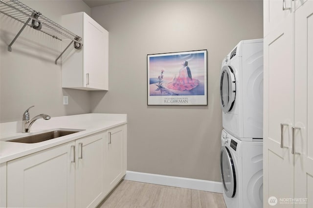 washroom featuring a sink, baseboards, cabinet space, light wood finished floors, and stacked washer and clothes dryer