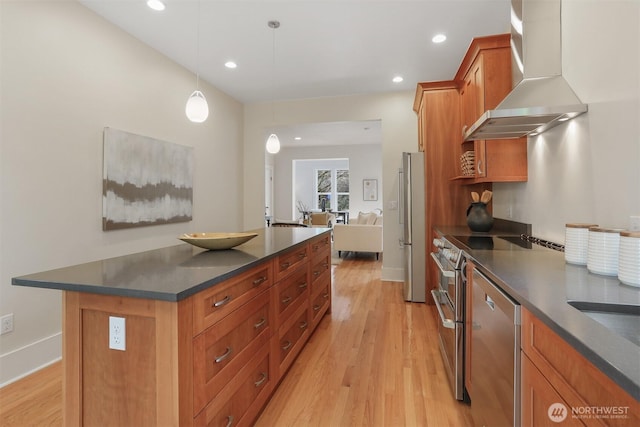 kitchen featuring dark countertops, wall chimney exhaust hood, light wood-style flooring, appliances with stainless steel finishes, and brown cabinets