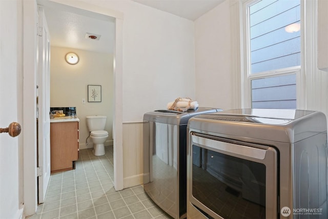 laundry room with laundry area, light tile patterned floors, a wainscoted wall, and washing machine and clothes dryer