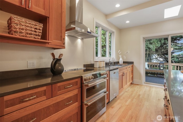 kitchen featuring a sink, appliances with stainless steel finishes, wall chimney exhaust hood, brown cabinetry, and dark countertops