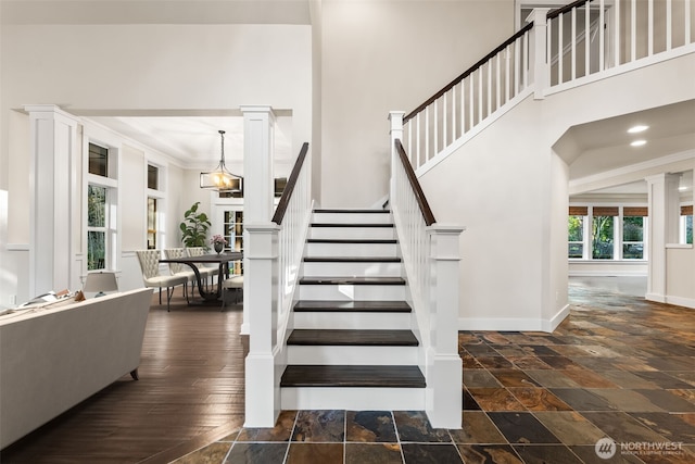 stairs featuring stone tile floors, ornate columns, a high ceiling, ornamental molding, and baseboards