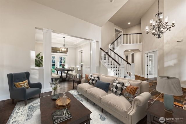 living area featuring a notable chandelier, wood finished floors, baseboards, stairway, and ornate columns