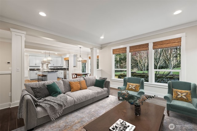 living room featuring ornamental molding, dark wood-type flooring, decorative columns, and an inviting chandelier